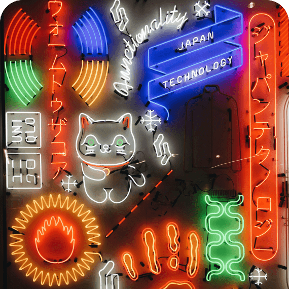 Colorful neon sign featuring a waving cat, Japanese characters, a blue ribbon with the words 'Japan Technology', and abstract neon shapes in red, green, orange, and blue on a dark background.